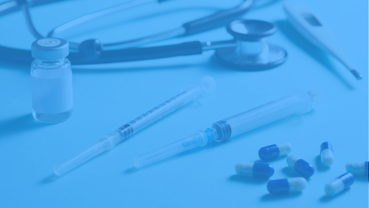Medical supplies including a stethoscope, vial, syringe, thermometer, and blue-and-white capsules on a blue background.
