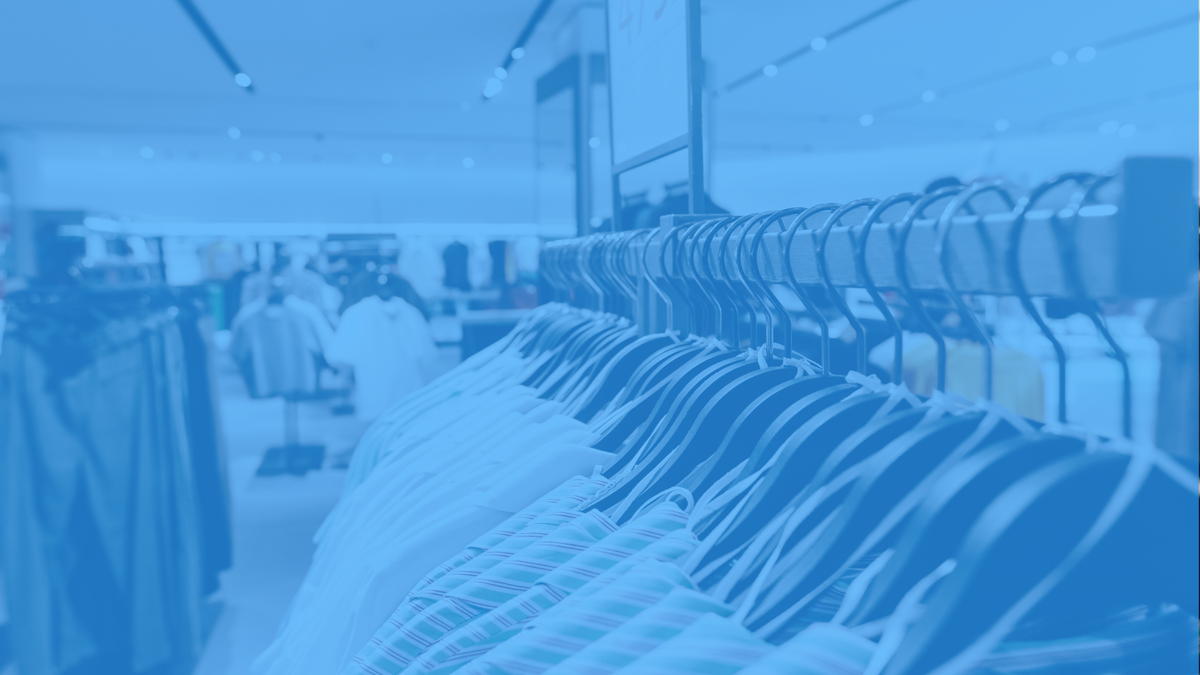 A blue-tinted, out-of-focus view of a clothing store interior with racks of garments in the foreground.